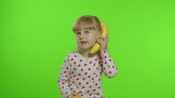 Happy child girl kid imitating telephone conversation with banana isolated on chroma key background video