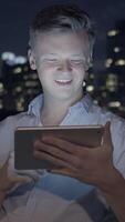 A Young Man Engaged in Using a Tablet Late at Night While Surrounded by an Urban Setting video
