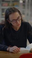 A focused woman is deeply engaged in reading at a table inside the library, surrounded by knowledge video