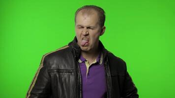 Aggressive rocker man in brown leather jacket showing tongue and looking with crazy expression video