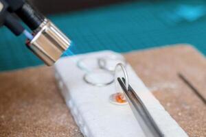 Detailed process of jewelry making with a torch on a white work surface in a creative studio. photo