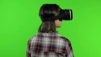 Young girl using VR app helmet to play simulation game. Woman watching virtual reality 3d video