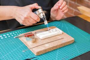 A woman uses a blowtorch to create jewelry on a on a worktable with cutting mat. photo