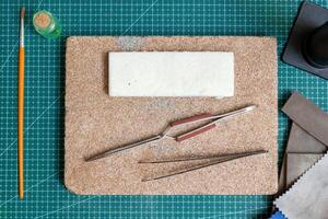 Tools for crafting handmade jewelry on green cutting mat - tweezers, foam block and sandpaper. photo