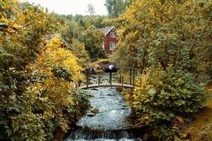 corriente con un pequeño puente en frente de un rojo de madera casa en Suecia en otoño. foto