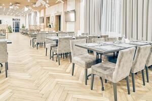 Side view of a large empty bright restaurant with tables, soft chairs, curtains and a wooden floor. Modern interior of a cafe, restaurant for events, holidays, weddings, birthdays with copy space photo