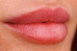 A close up of a womans lips one month after the permanent makeup procedure. A soft pigment shade highlights their natural shape. photo