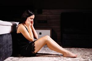 Unhappy woman touching hair, sitting on floor at home, thinking about problems. Upset girl feeling lonely and sad, psychological and mental troubles, suffering from bad relationship or break up photo