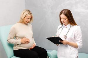 Gynecologist talking with a young female patient during a medical consultation in the gynecological office and and making entries in the patient's medical record photo