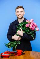 Man in apron cuts off the ends of a rose on blue background photo