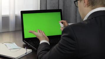 Man takes sanitizer bottle and use near laptop with green screen. Distance work video