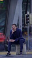 A contemplative man dressed in formal business attire is sitting outside, looking thoughtful video