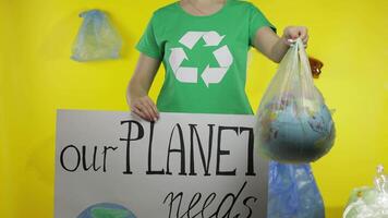 Unrecognizable woman with protesting poster and Earth globe in plastic package. Ecology pollution video