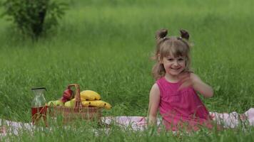 Weekend at picnic. Lovely caucasian child girl on green grass meadow sit on blanket waving her hands video