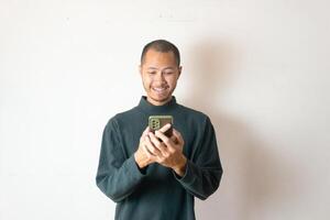 Young asian men wearing winter clothes or sweater is laughing while holding smartphone on isolated white photo