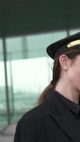 A confident female pilot dressed in a stylish uniform is smiling broadly at the airport video