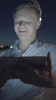 A Young Man is smiling joyfully at his device while enjoying a beautiful nighttime cityscape video