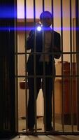 A mysterious figure investigates behind bars, using a flashlight to uncover hidden truths video
