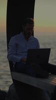 A man is working on his laptop while enjoying the ocean view during a beautiful sunset video