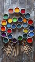 Open paint cans arranged in circle on rustic wooden table with paintbrushes photo