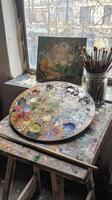 Artist palette resting on wooden table with paint brushes and abstract painting photo