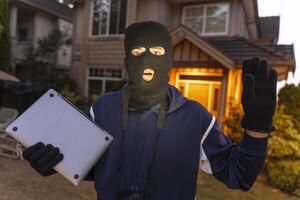 Surprised burglar holding laptop is getting caught red handed in front of house photo