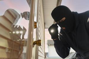 Masked burglar breaking into house at night using flashlight photo