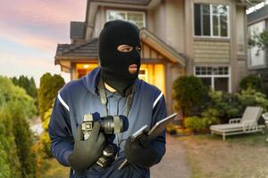 Masked burglar casing a house at dusk with camera and tablet photo
