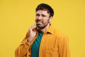Portrait of middle aged man wearing yellow casual shirt touching face, toothache photo