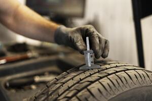 Mechanic measuring tyre tread depth using caliper photo