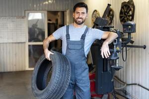 Mechanic holding a tire and smiling in a mechanical workshop photo