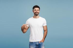 Portrait of handsome, smiling, bearded man wearing stylish white t shirt, pointing finger, mock up photo