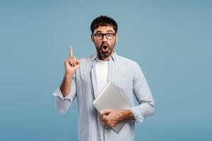 Excited attractive bearded man programmer having good idea finger up isolated on blue background photo