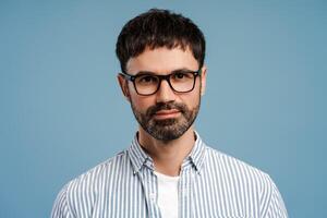 Pensive, smiling Latin man wearing stylish eyeglasses, looking at camera isolated on blue background photo
