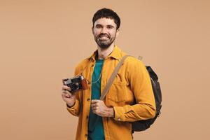 Portrait of smiling, happy bearded man, hipster holding backpack and camera traveling photo