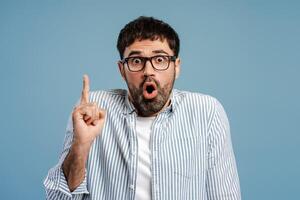 Excited bearded man holding finger up, wearing stylish eyeglasses with open mouth looking at camera photo