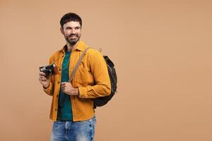 Portrait of smiling, handsome bearded man hipster holding backpack and camera traveling looking away photo