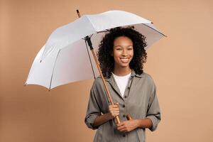 Curly African American woman with umbrella for fall season in studio on beige background photo