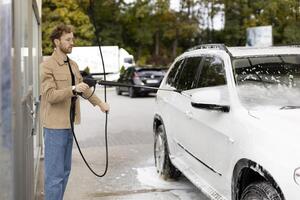 Man washing his car with a high pressure washer at a self service car wash photo