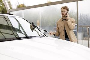 Stylish man washing his car while talking on the phone at a self service car wash photo