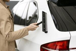 Man cleaning car window with squeegee after washing photo