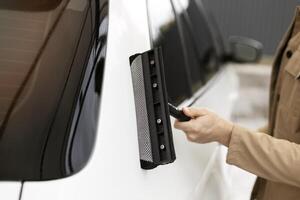 Professional car window cleaner using squeegee on vehicle during detailing service photo