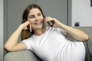 Young woman relaxing on sofa is talking on smartphone photo