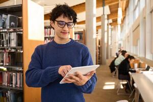 Young man using digital tablet while standing in library photo