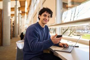 University student working on laptop and using smartphone in library photo