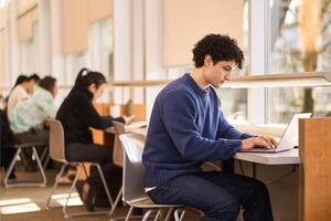 Focused student working on laptop in busy college library photo
