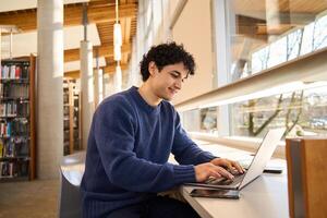 Smiling student working on laptop in university library photo