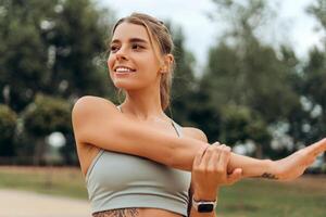 Smiling, beautiful woman wearing sport top warming up, stretching, looking away, doing exercise photo