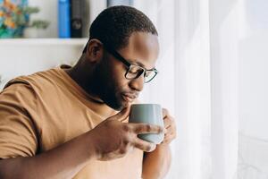 Handsome African American man in glasses drinking coffee at home photo