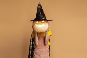 Unrecognizable kid wearing witch hat holding halloween pumpkin in front of her face photo